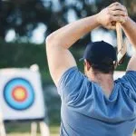 Man axe throwing at sports range, archery training or practice with board circle for action, game and fitness. Strong person with weapon for tomahawk competition, gaming and park or field with target