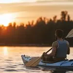 Vista trasera de hombre montando kayak en río al atardecer.