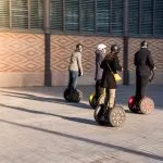 Grupa ludzi na ekologicznych hulajnogach Segway na zabytkowej ulicy w Hiszpanii. Turyści korzystający ze skuterów elektrycznych.